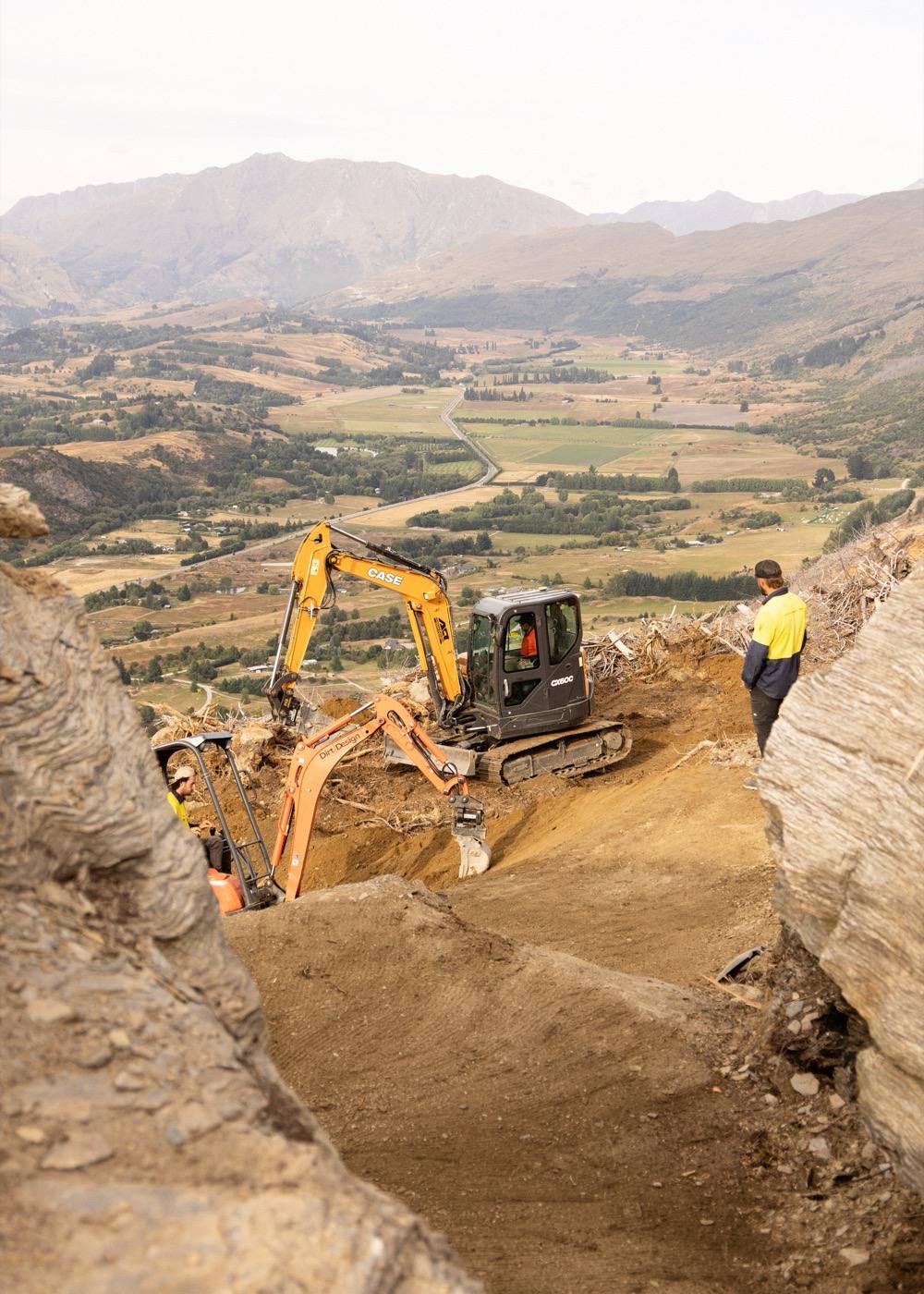Excavator working on trail construction with mountains in the background
