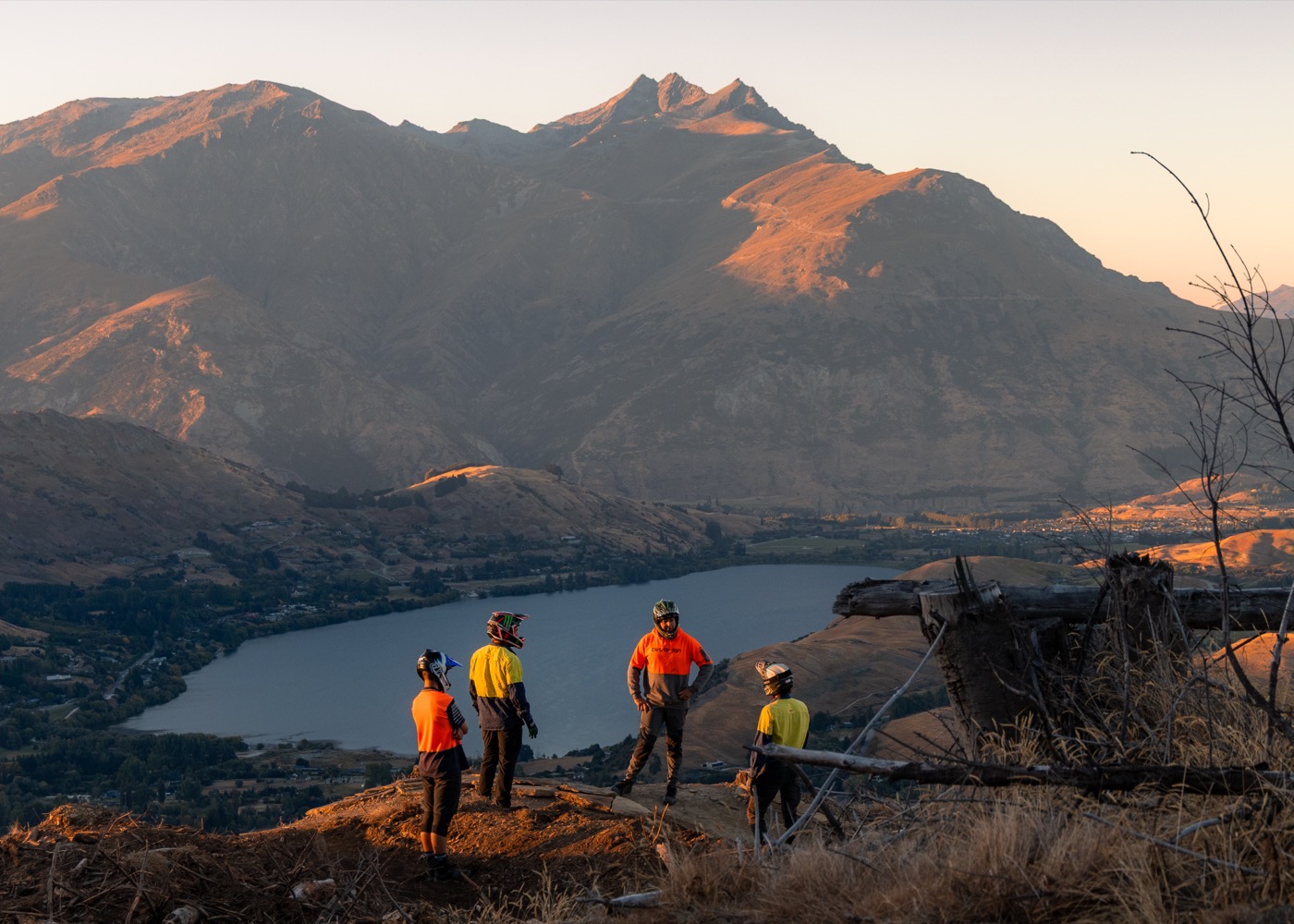 Riders at golden hour on a new alpine trail above Queenstown's lake and mountain range